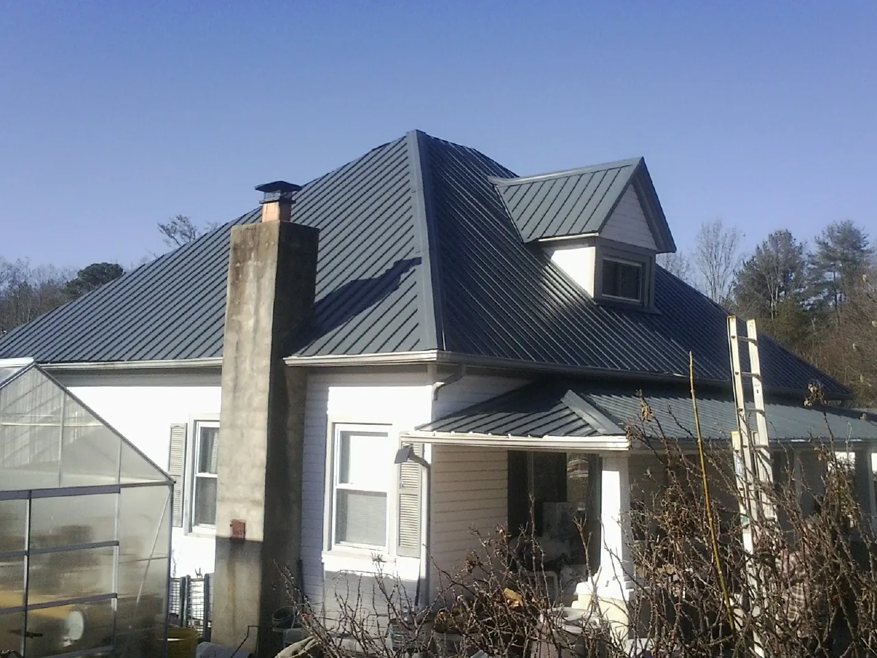 Dark blue standing seam metal roof on a white farmhouse with dormer — Slate & Tile Roof Repair by Roofing Brothers in Buckley