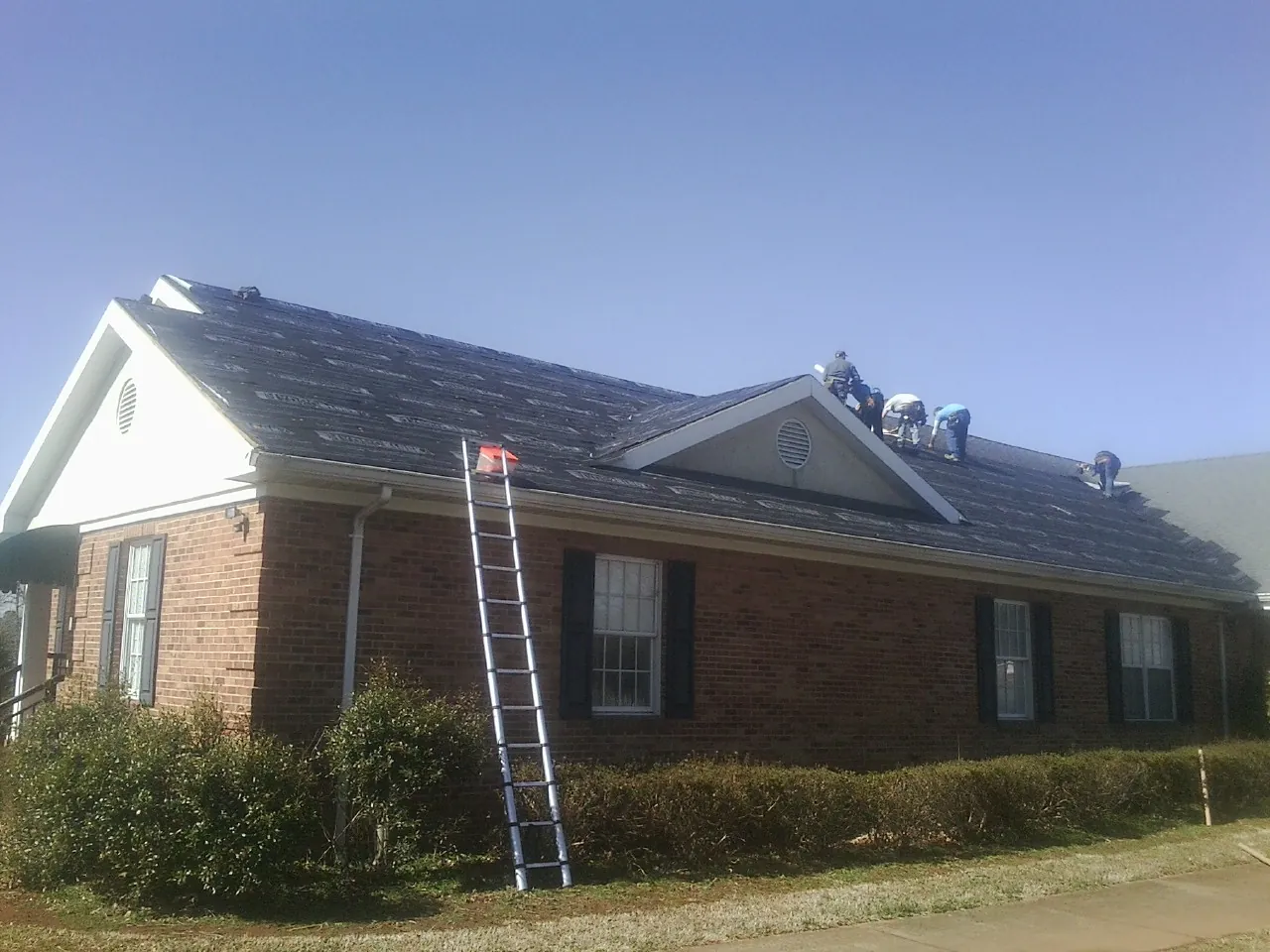 Crew tearing shingles off a brick ranch roof with a ladder set — Metal Roof Repair work by our crew in Buckley