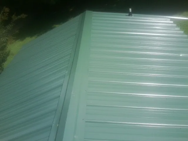 New green metal panels meeting at the ridge of a roof — Flat Roof Repair work by our crew in Buckley