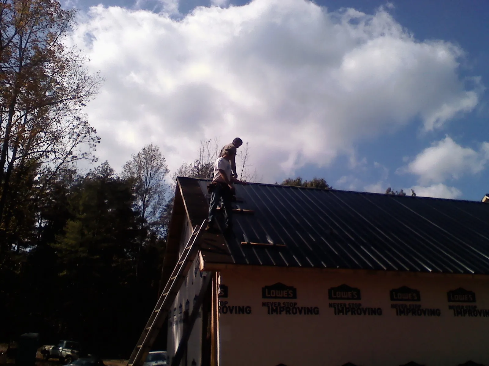 Roofer fastening dark metal panels high against a cloudy sky, from a Roof Inspection job in Buckley