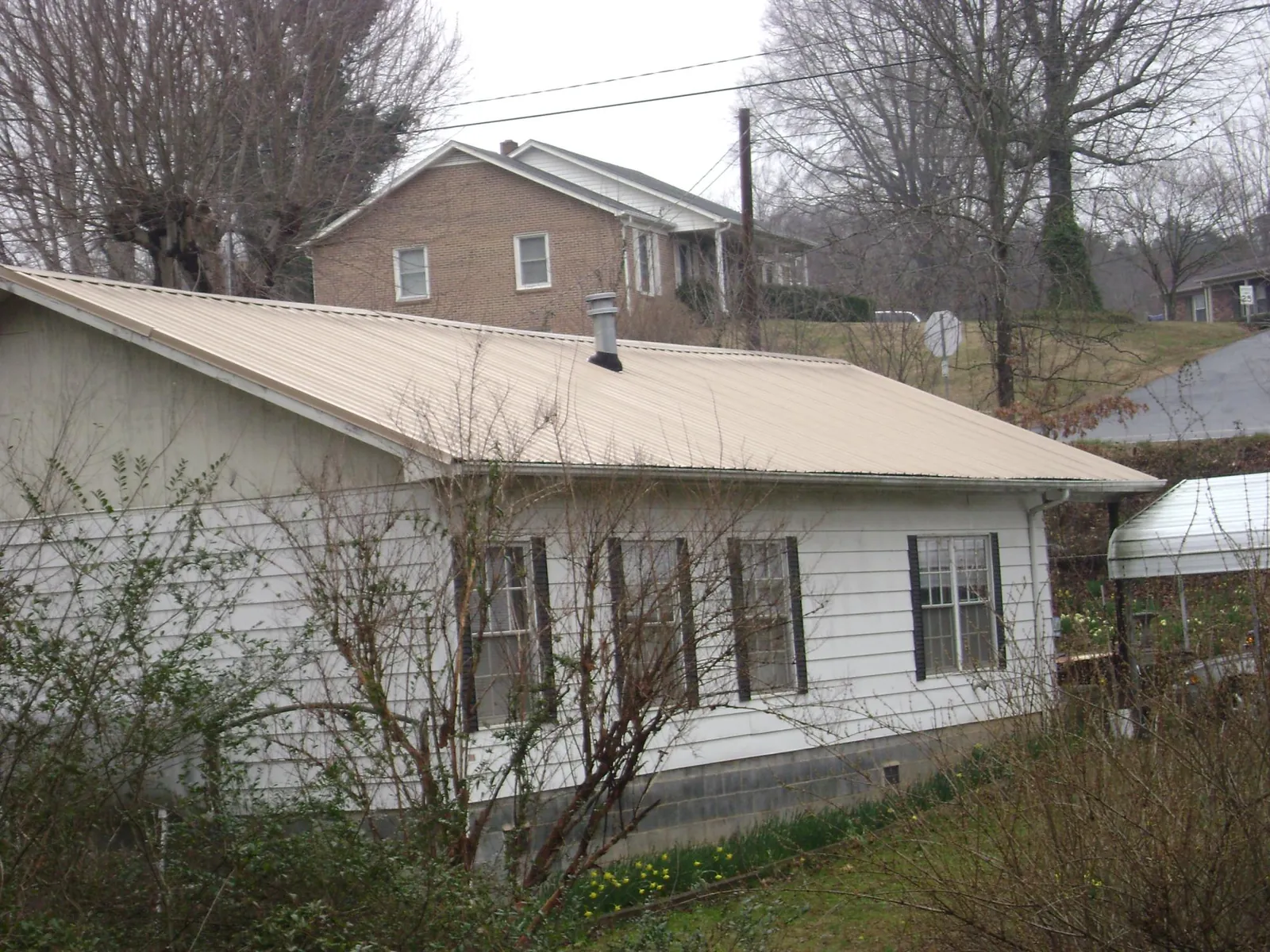 Tan metal roof on a white sided house set into a hillside — Commercial Roofing by Roofing Brothers in Buckley